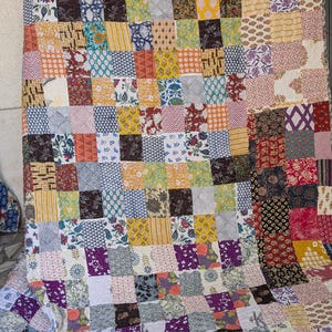 Puede incluir: Un edredón de retazos con una variedad de cuadrados de tela estampada en tonos de rojo, amarillo, azul, morado y verde. El edredón tiene una textura acolchada y un aspecto suave, ideal para una cama o un sofá.
