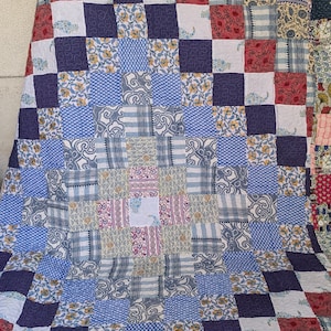 May include: A patchwork quilt with a variety of patterned squares in shades of blue, white, red, and yellow. The quilt features floral and geometric designs, creating a visually appealing textile. The quilt is likely made of cotton.