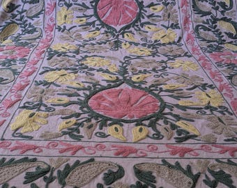 May include: A lavender textile with detailed embroidery. The design incorporates floral and paisley patterns in pink, yellow, green, and grey. A large pink flower surrounded by green leaves forms the central design.