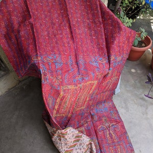 May include: A red, blue, and yellow kantha quilt with a paisley pattern. The quilt is made of recycled saris and is hand-stitched.