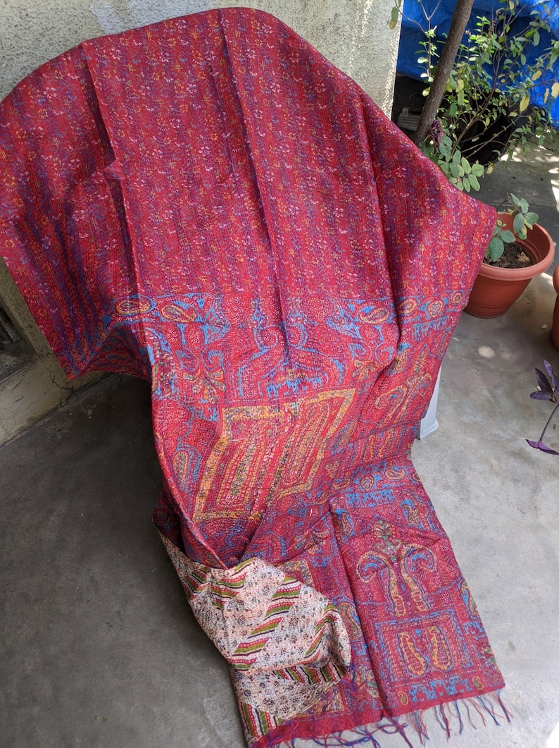 May include: A red, blue, and yellow kantha quilt with a paisley pattern. The quilt is made of recycled saris and is hand-stitched.