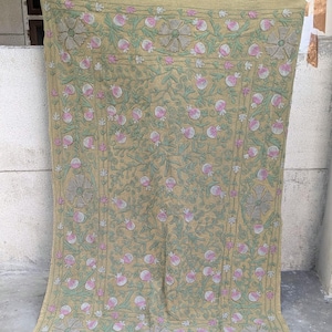 May include: A beige textile with an embroidered floral pattern. The design features pink and white flowers, green leaves, and grey accents. The textile is hanging, showing its full length and intricate details.