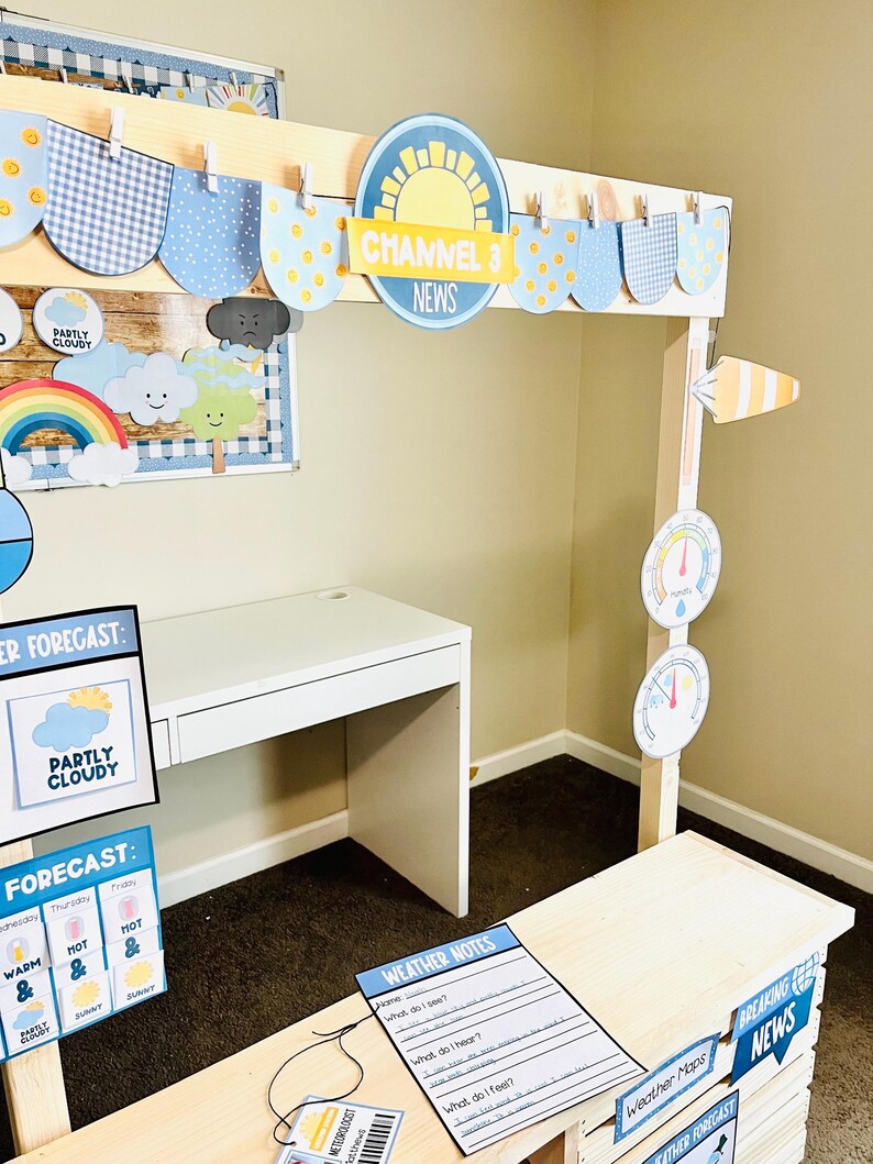 May include: A children's weather station play set with a white desk, a wooden news desk, and various weather-themed decorations. The set includes signs with the text "Channel 3 News", "Weather Forecast", and "Breaking News".