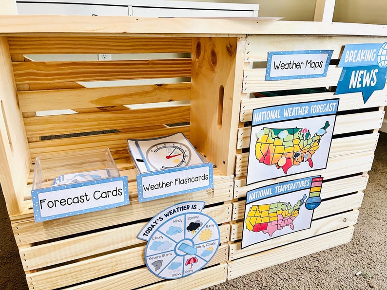 May include: A wooden weather station with various weather-related educational materials. It includes signs that read "Weather Maps," "Breaking News," "Forecast Cards," and "Weather Flashcards." The station also features a weather wheel and maps.