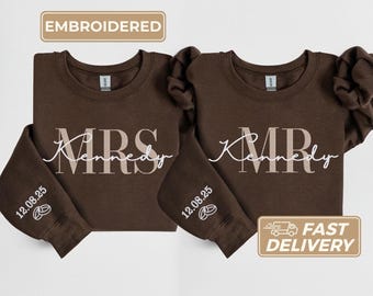 Peut inclure: Deux sweat-shirts marron avec texte brodé blanc. L'un dit "MRS Kennedy" et l'autre "MR Kennedy". Les manches portent la date "12.08.25" et un petit motif. Le coin supérieur gauche porte le mot "EMBROIDERED".