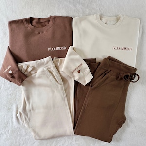 May include: Two sets of matching brown and cream colored sweatpants and sweatshirts. The sweatshirts have the text "IV.XX.MMXIV" on the front and the sweatpants have the text "I love you" and "I love you more" on the cuffs.