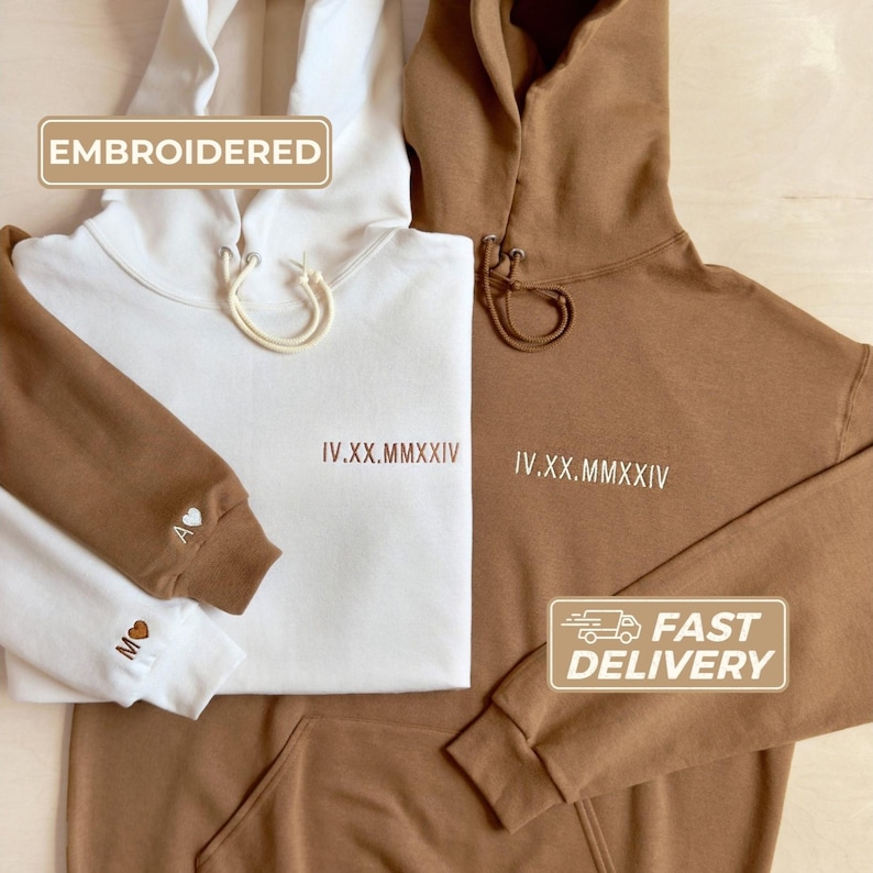 Custom embroidered anniversary hoodies. Sweet cream heather hoodie with golden pecan thread pictured on the left. Golden pecan hoodie with sweet cream thread pictured on the right. Custom date on chest. Custom initial with heart on sleeve.