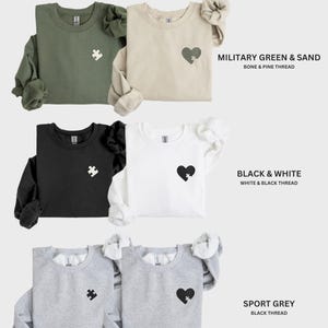 K&ouml;nnte beinhalten: Bild zeigt Sweatshirts in verschiedenen Farben: Milit&auml;rgr&uuml;n, Sand, Schwarz, Wei&szlig; und Sportgrau. Jedes Sweatshirt hat ein Herz- oder Puzzleteil-Design. Der Text "Bestselling Color Combinations" steht oben, mit Farbkombinationen und Fadendetails darunter.