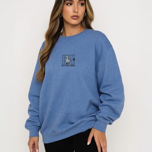 K&ouml;nnte beinhalten: Blaues Sweatshirt mit einem Enten-Grafik hinter Gittern und dem Text "got too silly". Das Sweatshirt hat eine blaue Farbe und lange &Auml;rmel. Das Model tr&auml;gt schwarze Shorts.