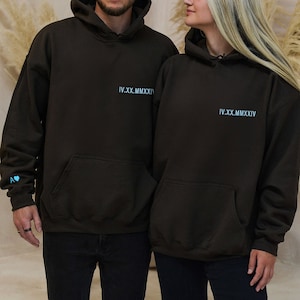 Puede incluir: Dos sudaderas con capucha marrones con el texto "IV.XX.MMXIV" impreso en la parte delantera. La sudadera de la izquierda tiene un peque&ntilde;o coraz&oacute;n azul en la manga.