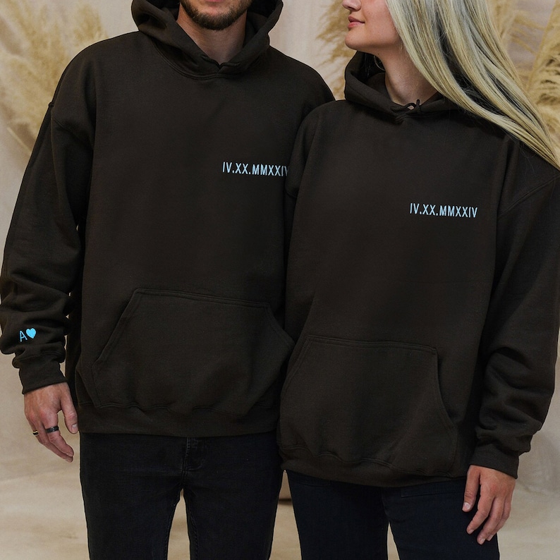 Puede incluir: Dos sudaderas con capucha marrones con el texto "IV.XX.MMXIV" impreso en la parte delantera. La sudadera de la izquierda tiene un peque&ntilde;o coraz&oacute;n azul en la manga.