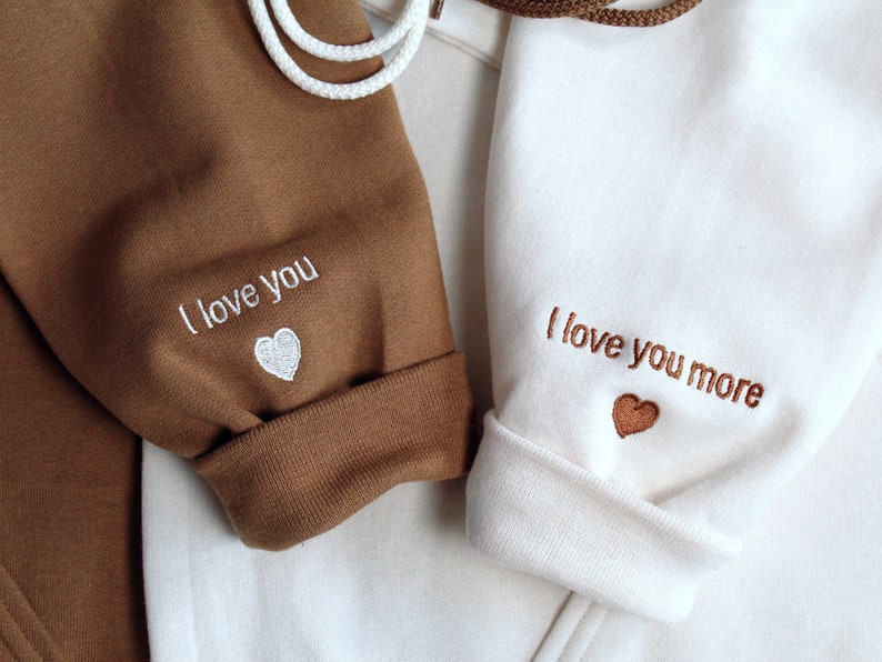 Engagement gift for couple shown. I love you / te amo embroidered with heart on sleeve on left. I love you more / te amo mas example shown on sleeve on right. Custom initial and text or phrase or wording on sleeve.