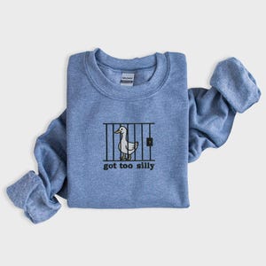 K&ouml;nnte beinhalten: Hellblaues Sweatshirt mit Rundhalsausschnitt und gerollten &Auml;rmeln. Auf der Vorderseite befindet sich eine Grafik einer Ente hinter Gittern mit dem Text "got too silly" in Schwarz. Das Sweatshirt ist aus weichem Material.