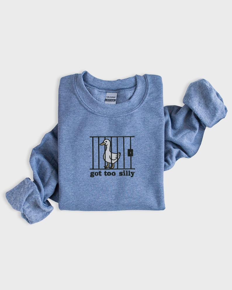 K&ouml;nnte beinhalten: Hellblaues Sweatshirt mit Rundhalsausschnitt und gerollten &Auml;rmeln. Auf der Vorderseite befindet sich eine Grafik einer Ente hinter Gittern mit dem Text "got too silly" in Schwarz. Das Sweatshirt ist aus weichem Material.