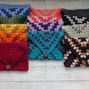 May include: A stack of 10 crocheted envelopes in various colors, including red, orange, yellow, green, blue, purple, brown, and gray. Each envelope has a button closure.