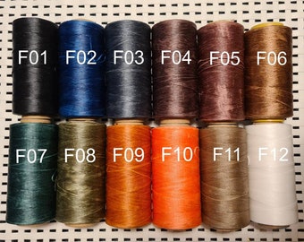 Pode incluir: Uma coleção de doze carretéis de linha em várias cores, incluindo preto, azul marinho, castanho, laranja e branco. Cada carretel é rotulado com um número "F" correspondente, variando de F01 a F12.
