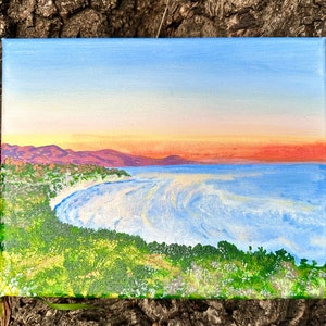 Puede incluir: Una pintura de una escena costera con un cielo azul, una puesta de sol naranja y una ladera verde que domina un océano azul con olas blancas.