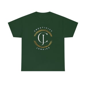 Puede incluir: Una camiseta verde oscuro con un logotipo circular dorado y blanco. El logotipo presenta las palabras "CREATIVITY JUNKIES" y las letras "CJ". El logotipo tiene un efecto de purpurina dorada. La camiseta está hecha de un material suave.