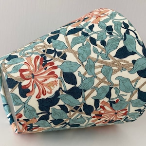 May include: A white lampshade with a floral pattern featuring blue, green, and orange flowers. The pattern is reminiscent of a vintage design.