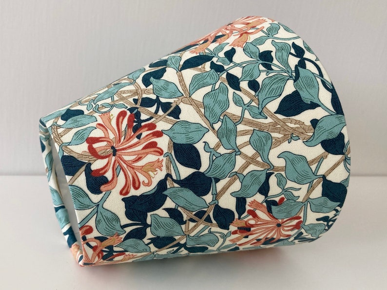 May include: A white lampshade with a floral pattern featuring blue, green, and orange flowers. The pattern is reminiscent of a vintage design.