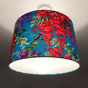 Op de afbeelding: Een blauwe lampenkap met een bloemenpatroon met roze, rode en paarse bloemen. De lampenkap heeft een witte binnenkant.