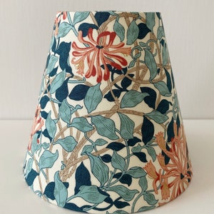 May include: A white lampshade with a floral pattern featuring blue, green, and orange flowers. The lampshade is cone-shaped and has a white background.