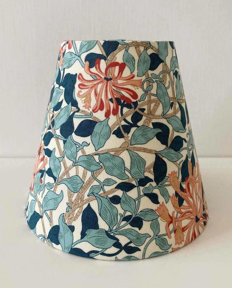 May include: A white lampshade with a floral pattern featuring blue, green, and orange flowers. The lampshade is cone-shaped and has a white background.