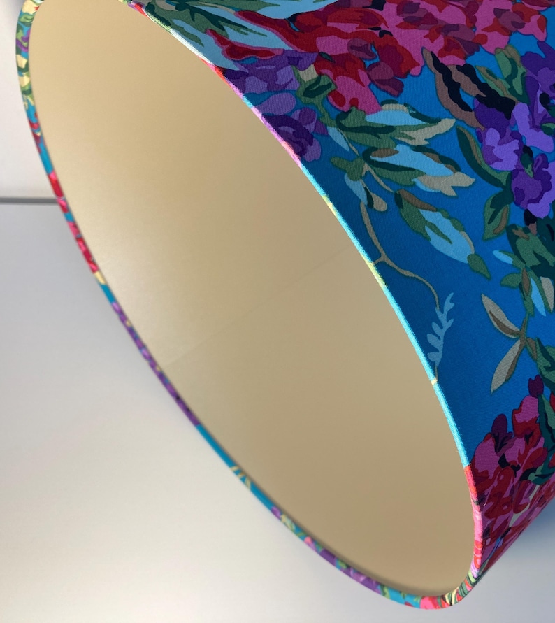 Op de afbeelding: Een close-up van een lampenkap met een bloemenpatroon. De lampenkap is gemaakt van stof en heeft een cr&egrave;mekleurige voering. Het bloemenpatroon is in tinten roze, paars en blauw op een turquoise achtergrond.