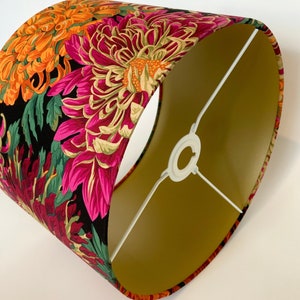 May include: A lampshade with a black background and a floral pattern in shades of pink, orange, and green. The lampshade has a gold lining.