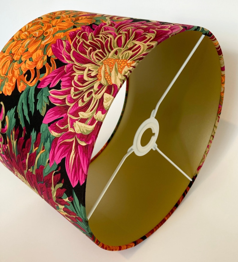 May include: A lampshade with a black background and a floral pattern in shades of pink, orange, and green. The lampshade has a gold lining.