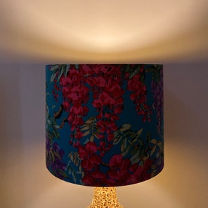 Op de afbeelding: Een tealblauwe lampenkap met een bloemenpatroon van roze en paarse bloemen. De lampenkap is gemaakt van stof en heeft een witte achtergrond.