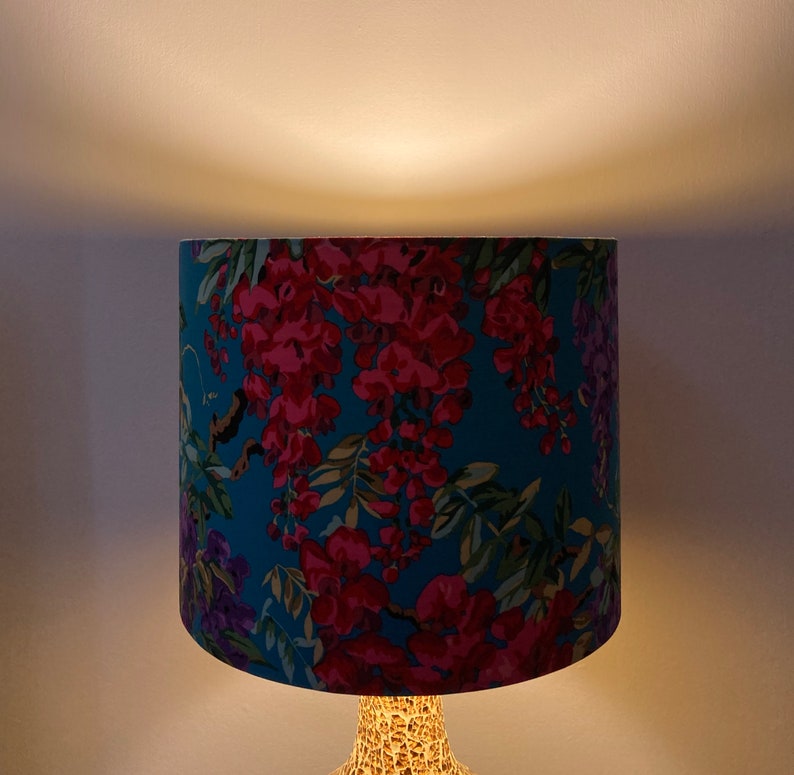Op de afbeelding: Een tealblauwe lampenkap met een bloemenpatroon van roze en paarse bloemen. De lampenkap is gemaakt van stof en heeft een witte achtergrond.