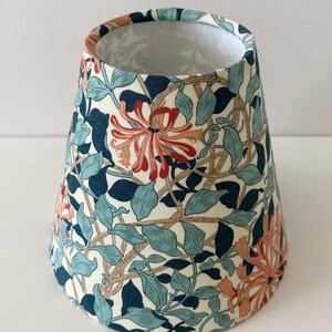 May include: A white lampshade with a floral pattern featuring blue, green, and orange flowers. The lampshade is cone-shaped and has a white lining.