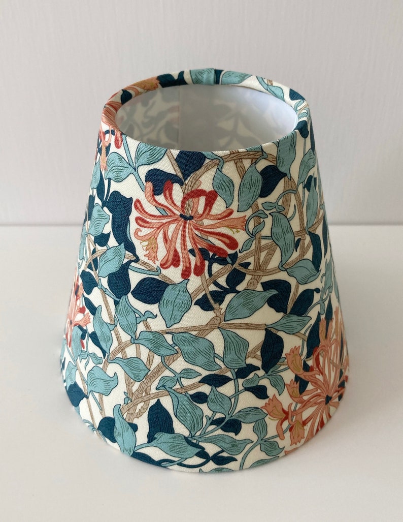 May include: A white lampshade with a floral pattern featuring blue, green, and orange flowers. The lampshade is cone-shaped and has a white lining.