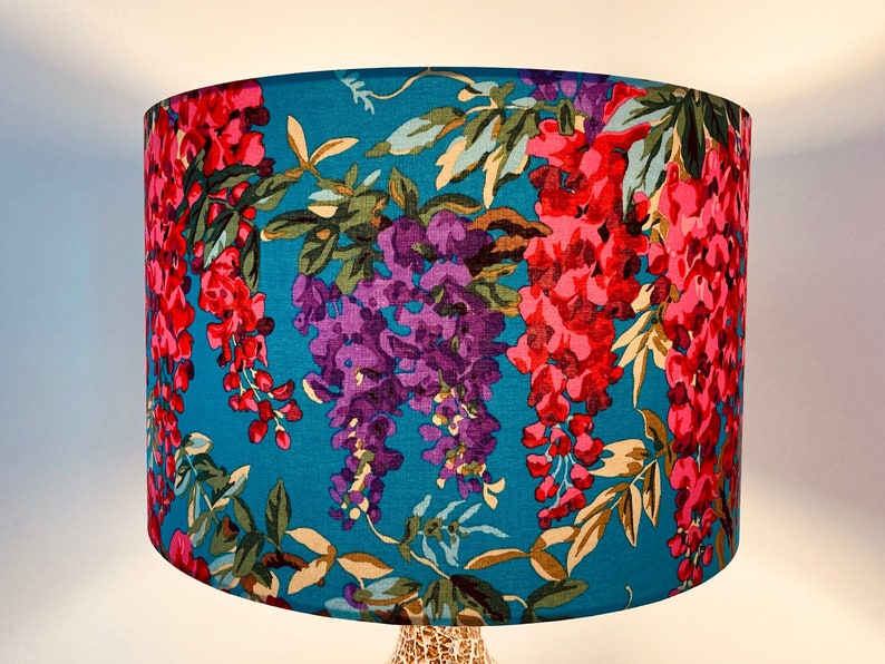 Op de afbeelding: Een tealblauwe lampenkap met een bloemenpatroon met roze en paarse blauwe regen bloemen.