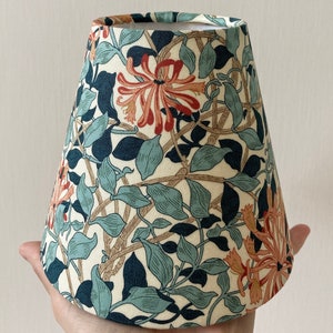 May include: A white lampshade with a floral pattern featuring blue, green, and orange flowers. The lampshade is cone-shaped and has a white lining.