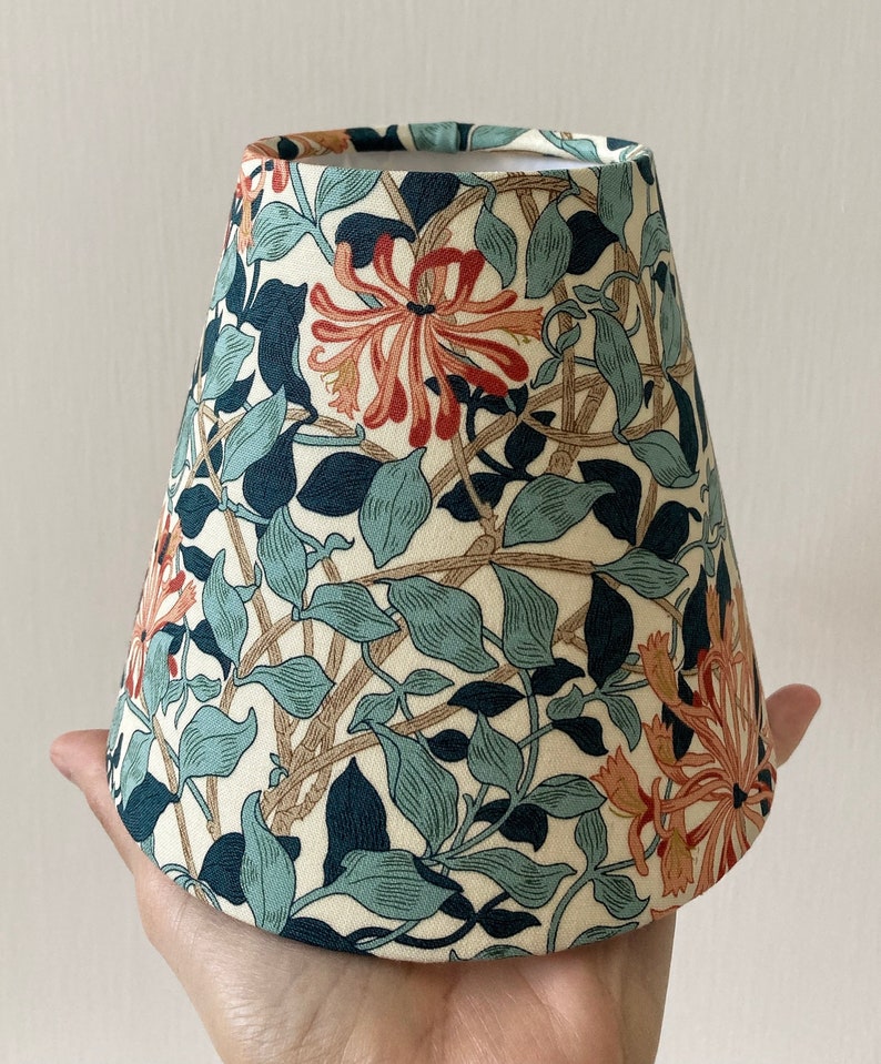 May include: A white lampshade with a floral pattern featuring blue, green, and orange flowers. The lampshade is cone-shaped and has a white lining.