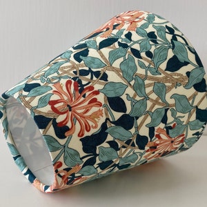 May include: A cream-colored lampshade with a floral pattern featuring blue, green, and orange flowers. The pattern is reminiscent of a vintage design.