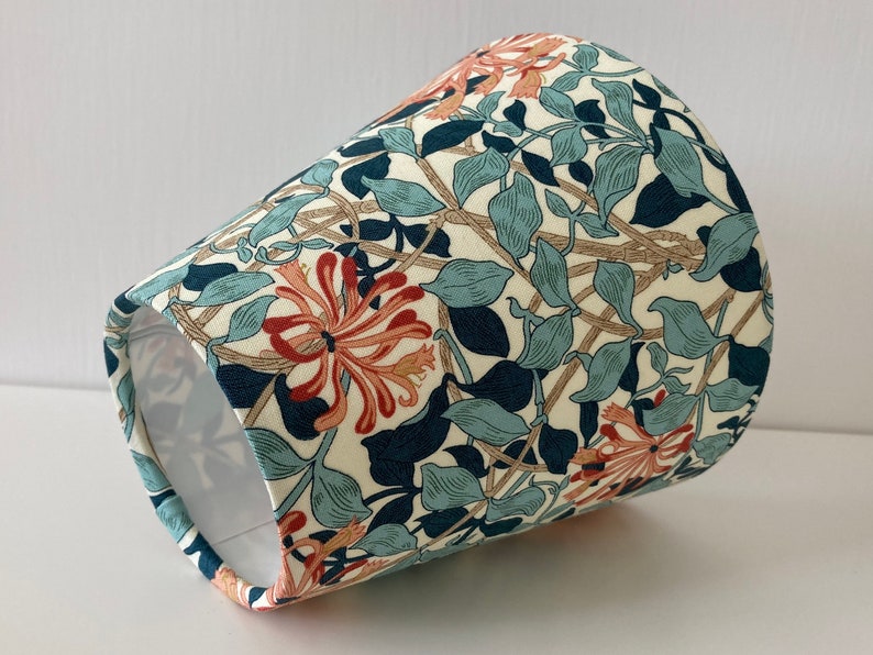 May include: A cream-colored lampshade with a floral pattern featuring blue, green, and orange flowers. The pattern is reminiscent of a vintage design.