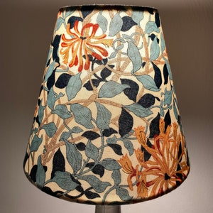 May include: A lampshade with a floral pattern featuring blue, green, orange, and brown hues. The pattern is reminiscent of honeysuckle vines.