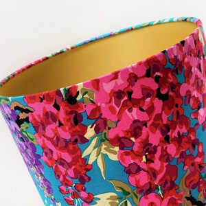 Op de afbeelding: Een lampenkap met een bloemenpatroon in tinten roze, paars en blauw op een turquoise achtergrond. De binnenkant van de lampenkap is effen geel.