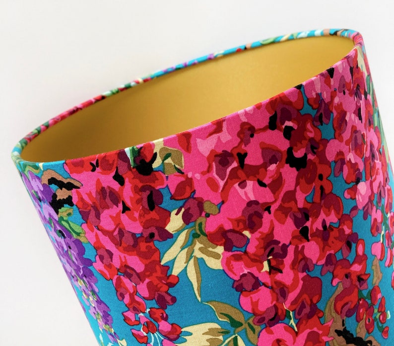 Op de afbeelding: Een lampenkap met een bloemenpatroon in tinten roze, paars en blauw op een turquoise achtergrond. De binnenkant van de lampenkap is effen geel.
