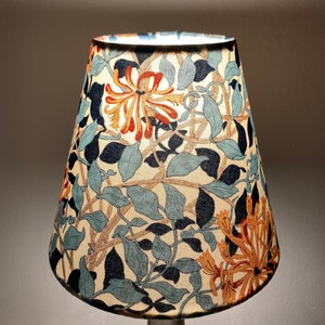 May include: A lampshade with a floral pattern featuring orange, blue, and green flowers on a cream background.