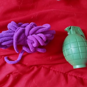 May include: A purple fuzzy yarn ball and a green plastic toy grenade on a red surface.
