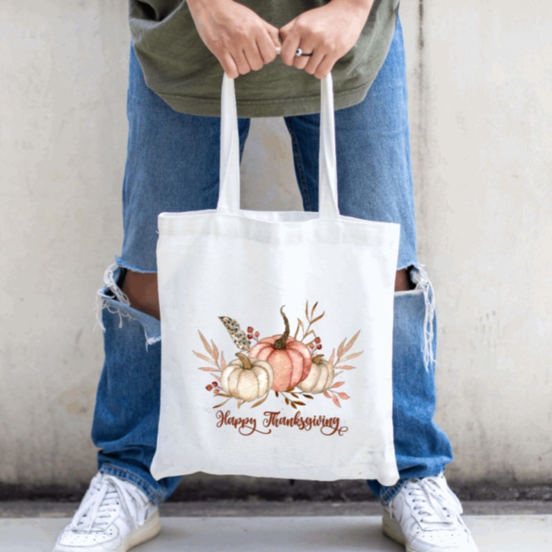May include: White canvas tote bag with a watercolor design of pumpkins, leaves, and berries. The text "Happy Thanksgiving" is printed in brown below the design.