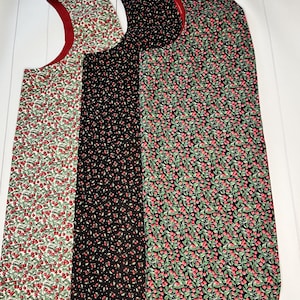 May include: Four bibs with a cherry pattern. The bibs have a red trim and are made of fabric. The patterns include cherries on a white background, cherries on a black background, and cherries on a dark green background.