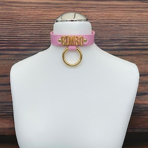 May include: Pink leather choker with a gold metal ring and the word "BIMBO" in gold lettering.