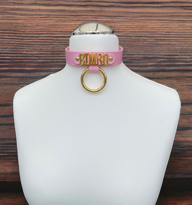 May include: Pink leather choker with a gold metal ring and the word "BIMBO" in gold lettering.