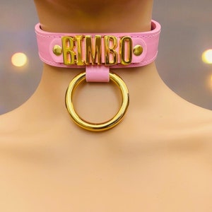 May include: Pink leather choker with a gold metal ring and the word "BIMBO" in gold letters.