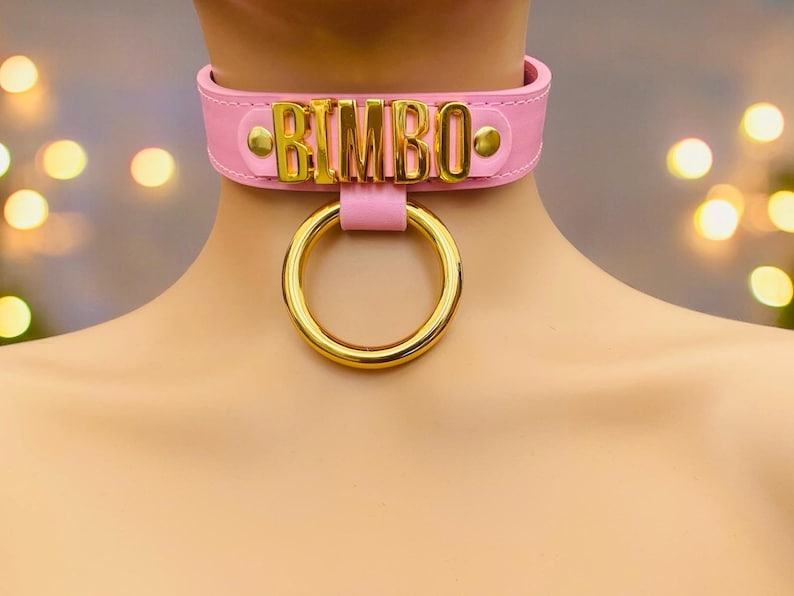 May include: Pink leather choker with a gold metal ring and the word "BIMBO" in gold letters.